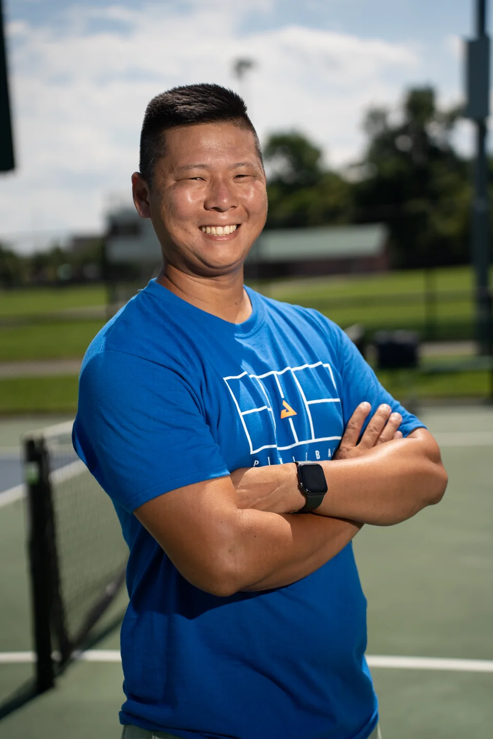 Sam Morris smiling with his arms folded on an outdoor court.