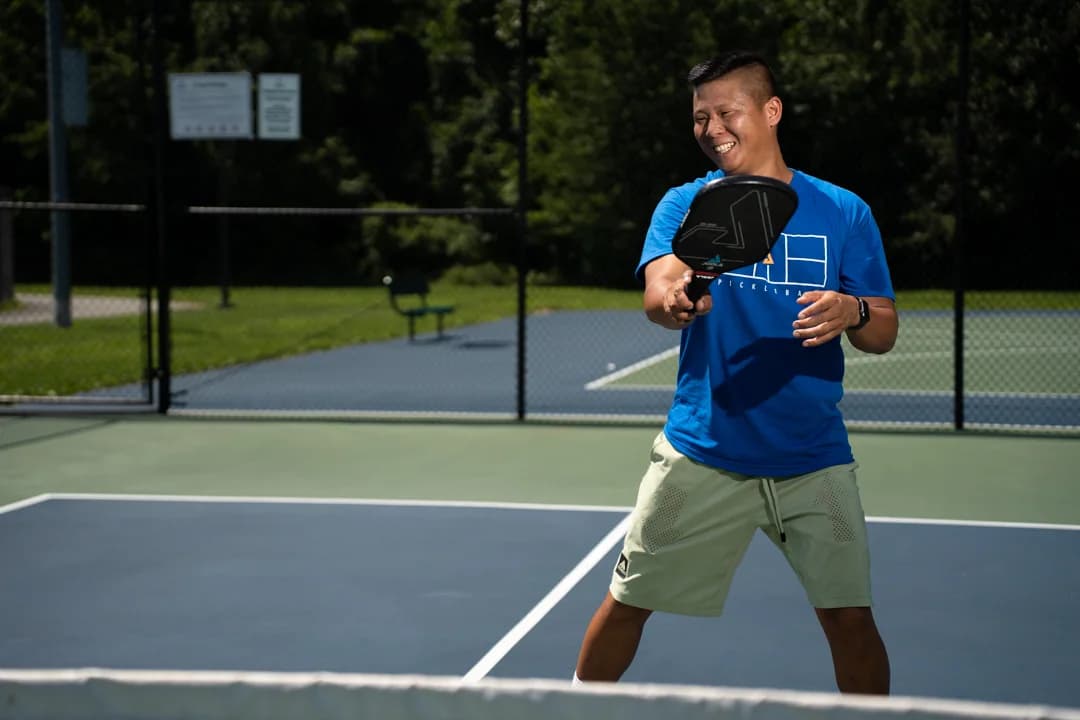 Sam Morris smiling during a paddle swing beside the pickleball net.