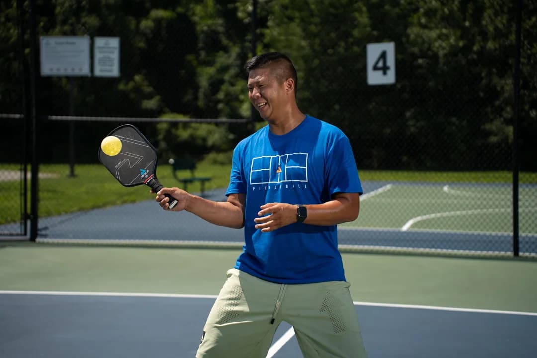 Sam Morris watching a yellow ball near his paddle on an outdoor court.