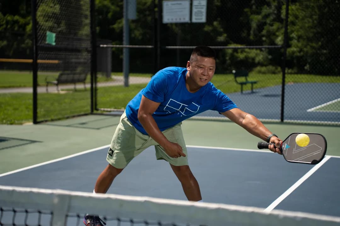 Sam Morris bending forward to reach a ball with his paddle near the net.